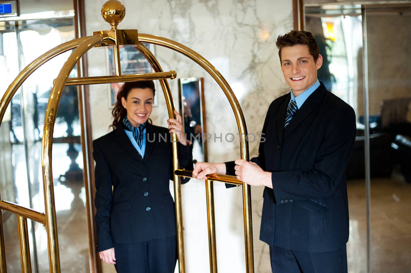 Concierges holding the cart and posing in front of the camera in hotel lounge