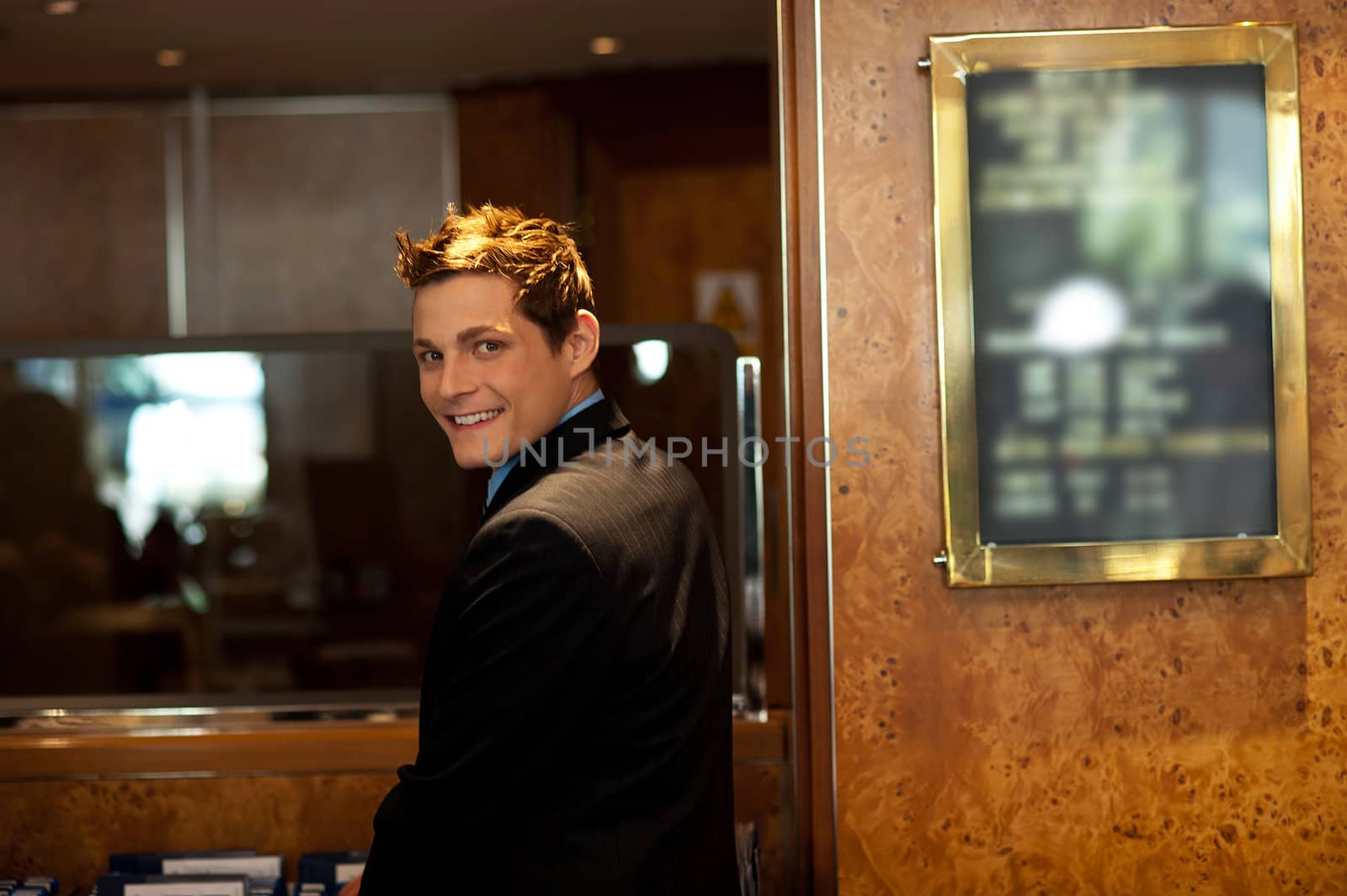 Attractive young guy turning back and looking at you. Indoors reception shot