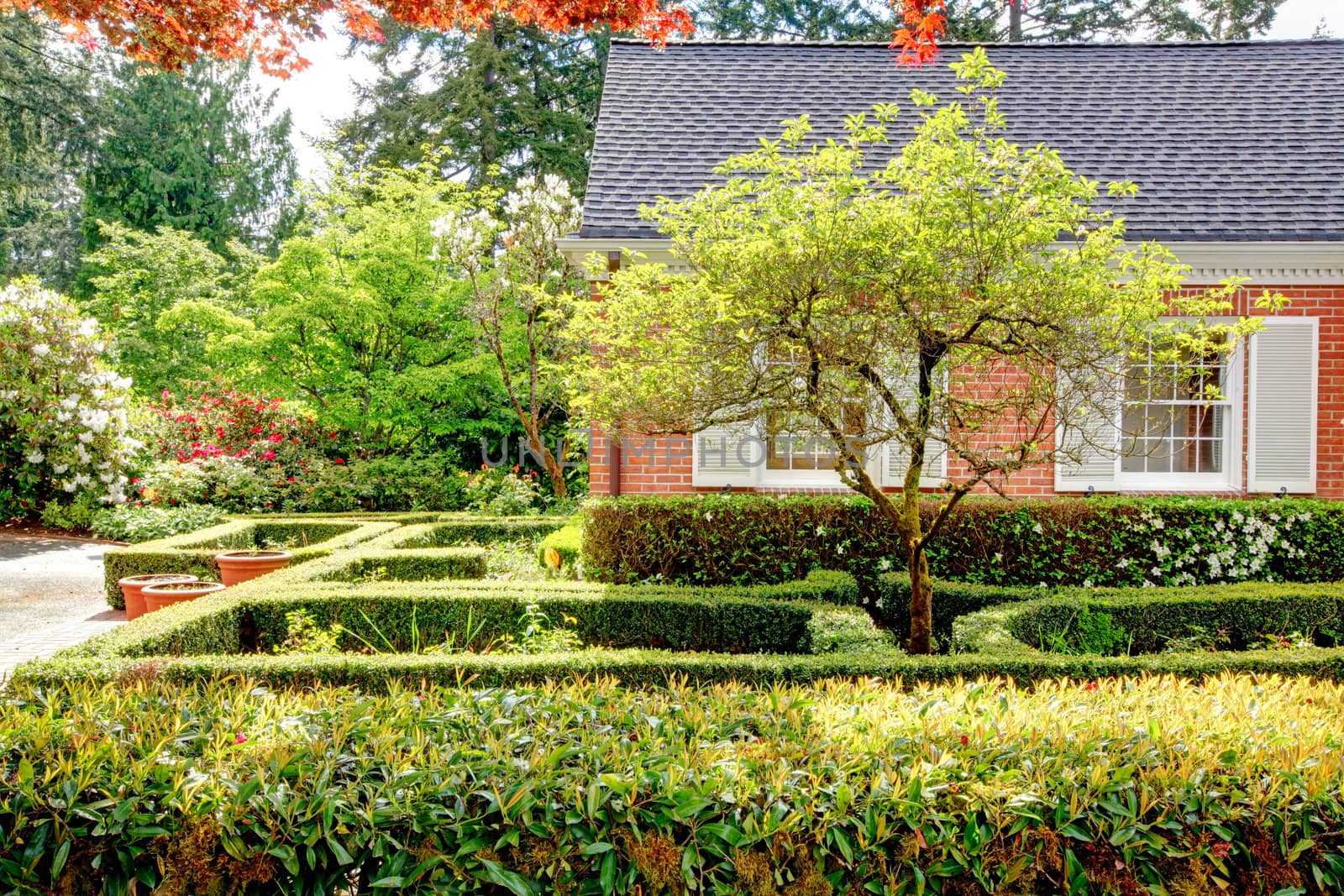 Brick red house with English garden and white window shutters. Summer landscape.