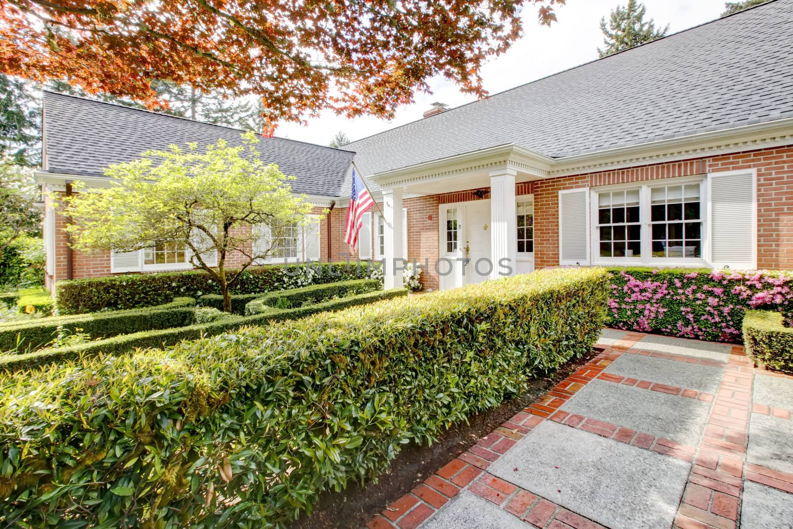 Brick red house with English garden and white window shutters. Summer landscape.