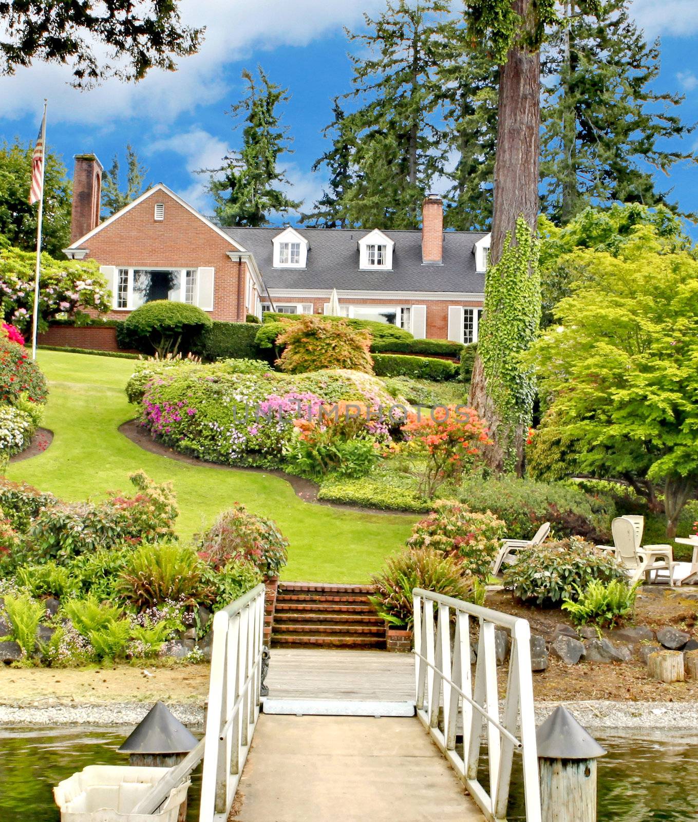 Brick red house with English garden and white window shutters. Summer landscape.