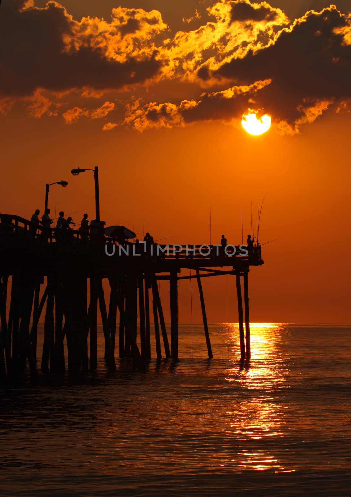 Early-morning anglers are silhouetted against the rising sun on a fishing pier in Nags Head, North Carolina vertical