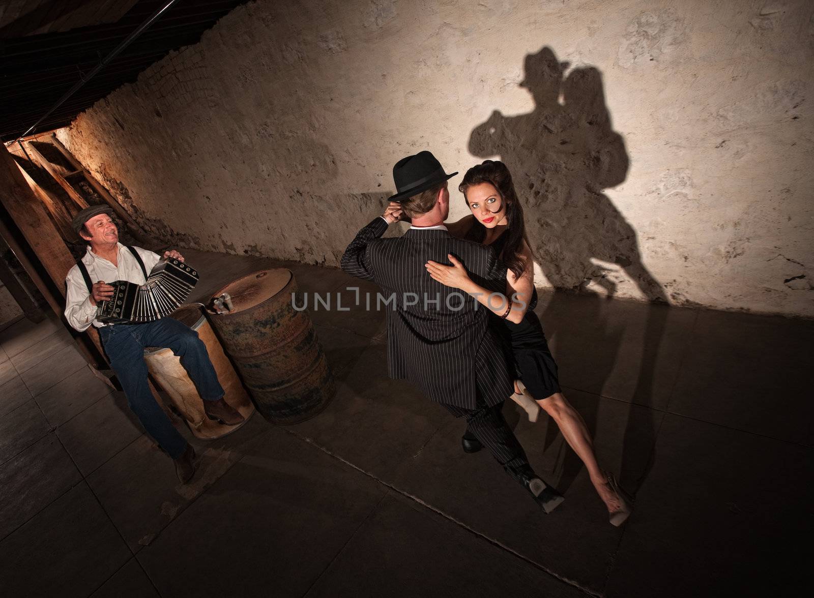 Tango dancers performing indoors with squeezebox player in background