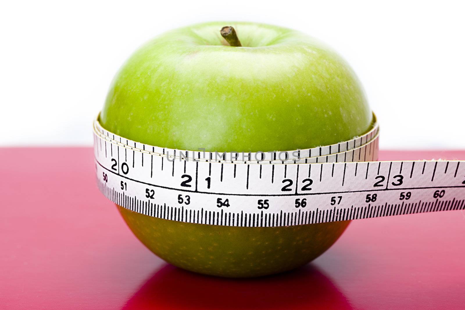 Shot of an apple on a table with a measuring tape around it.