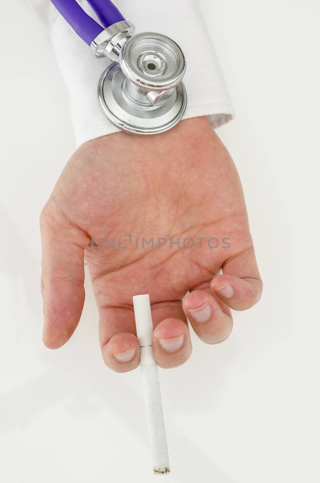 Stethoscope on a hand holding a cigarette on a white table.