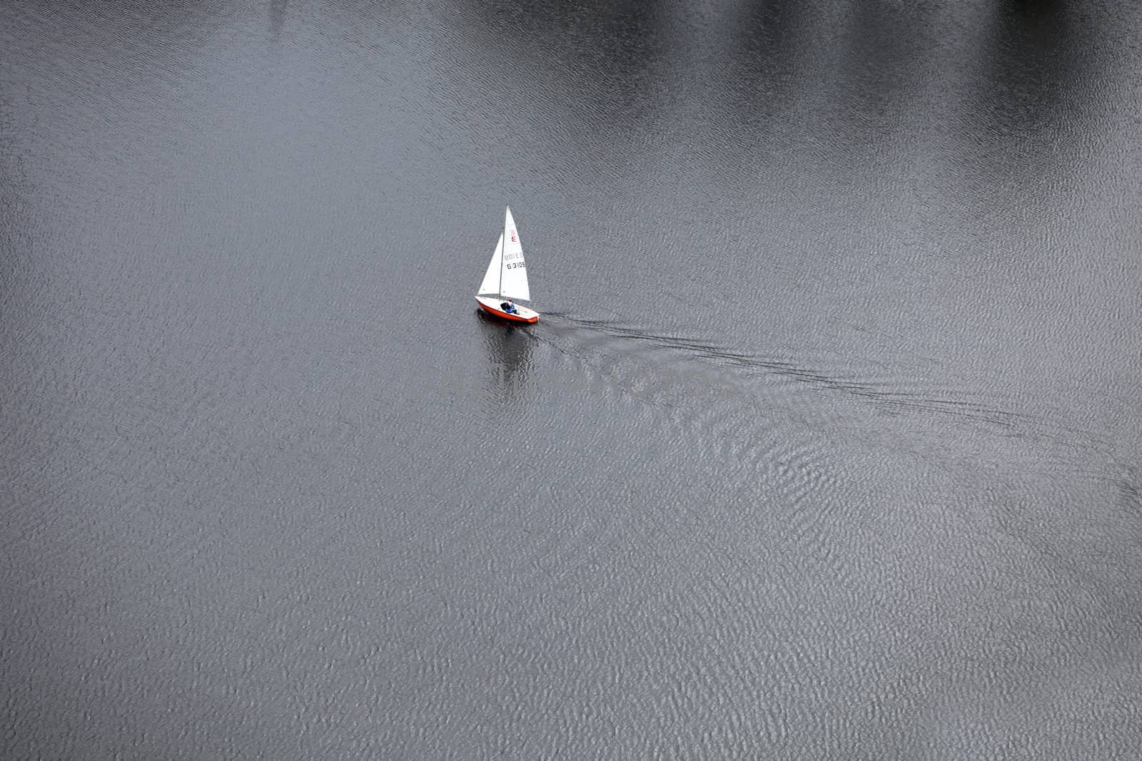 Aerial photograph of a white sailboat, sailing alone in the sea or river.