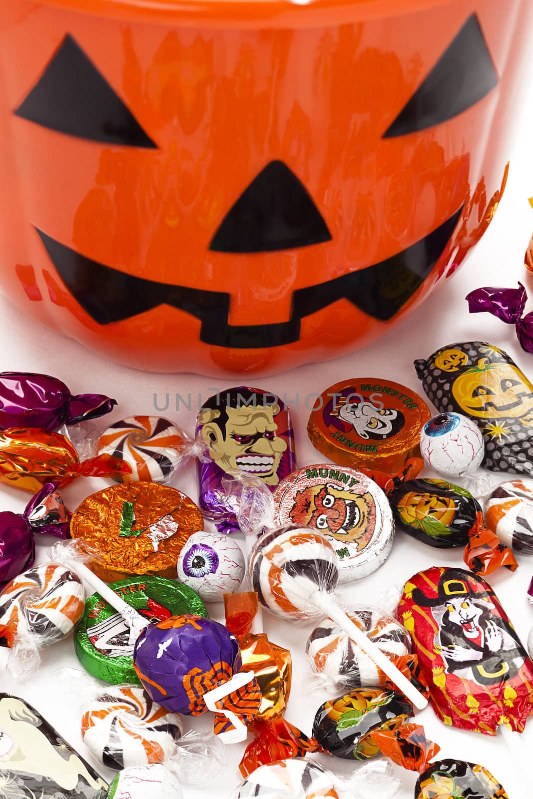 Small kid's jack o lantern bucket with candies in front.