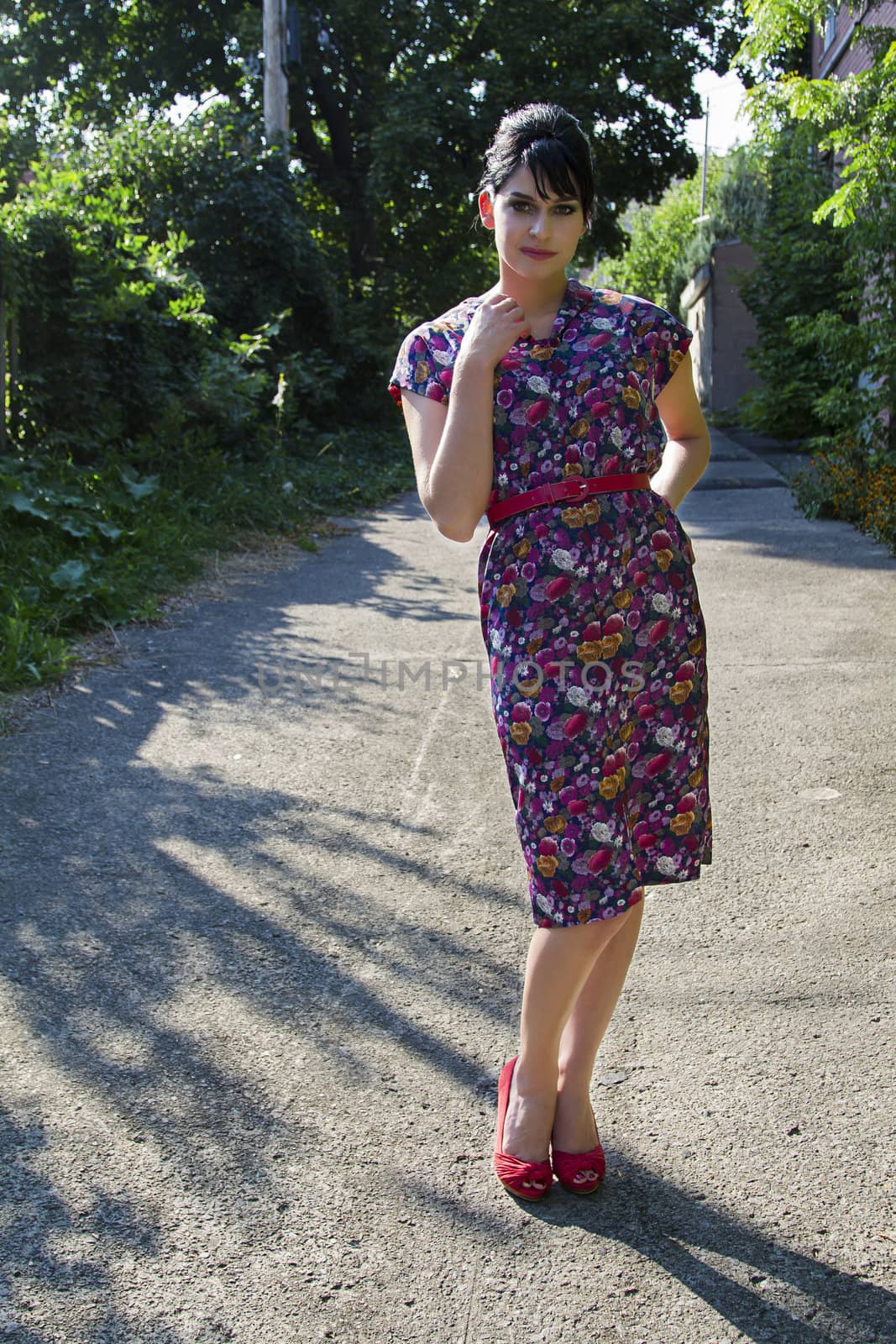 Young woman wearing a multi colored flower pattern dress posing in an urban alley