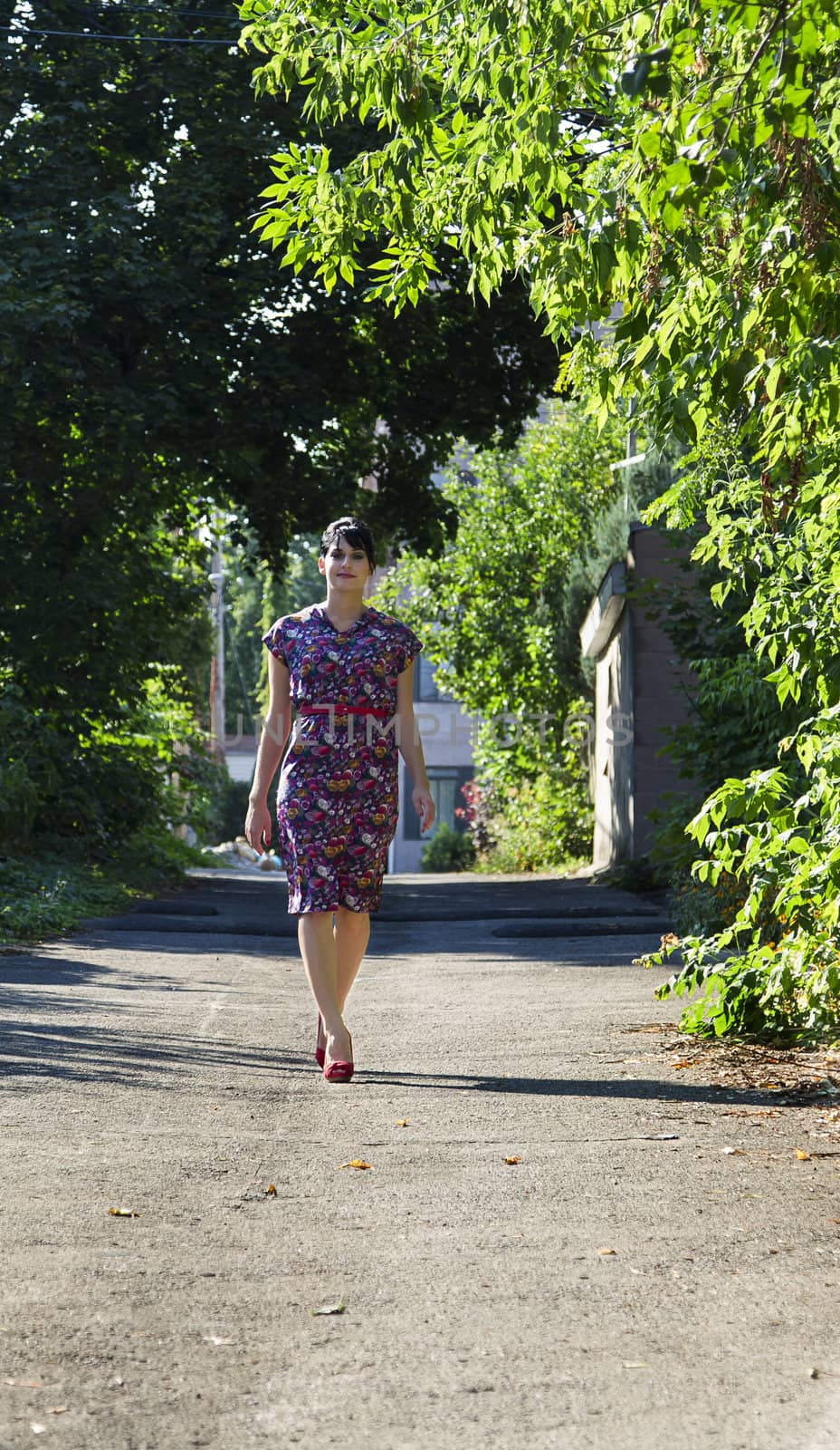 Young woman wearing a multi colored flower pattern dress walking in an urban alley