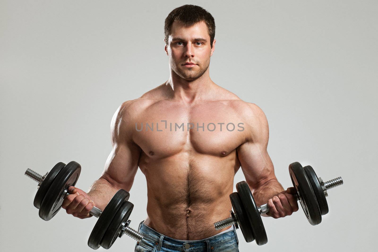 Handsome guy working out with dumbbells isolated over grey background