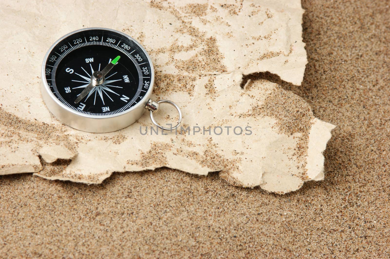 Compass on old sheet crumpled paper against the background of sand