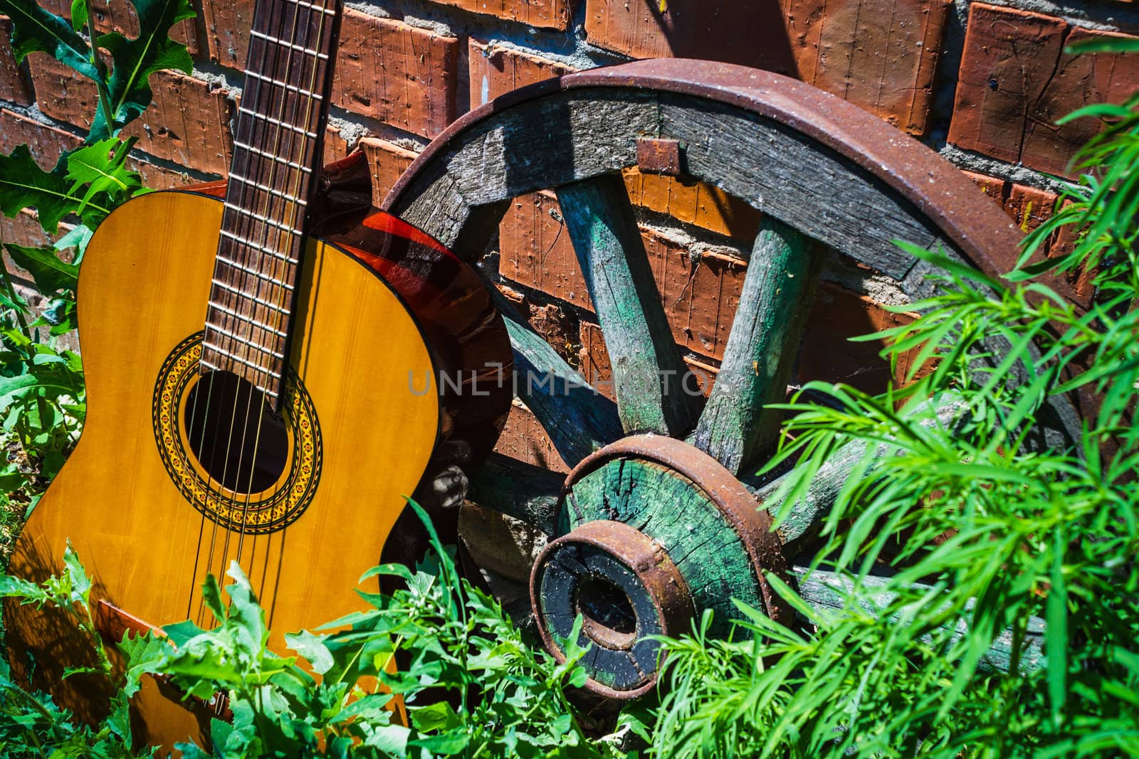 Guitar and the old wagon wheel against a brick wall