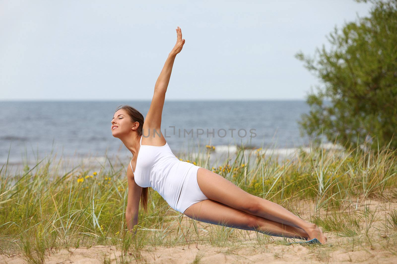 Beautiful caucasian woman making yoga at the beach near sea