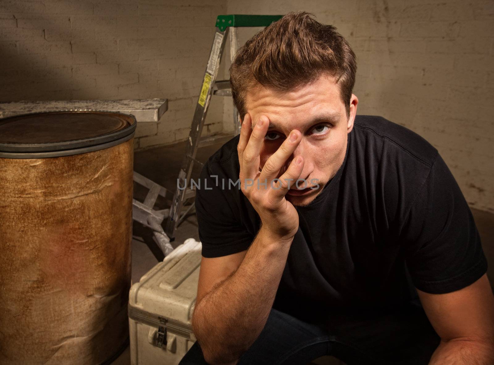 Unhappy young white man sitting on crate indoors