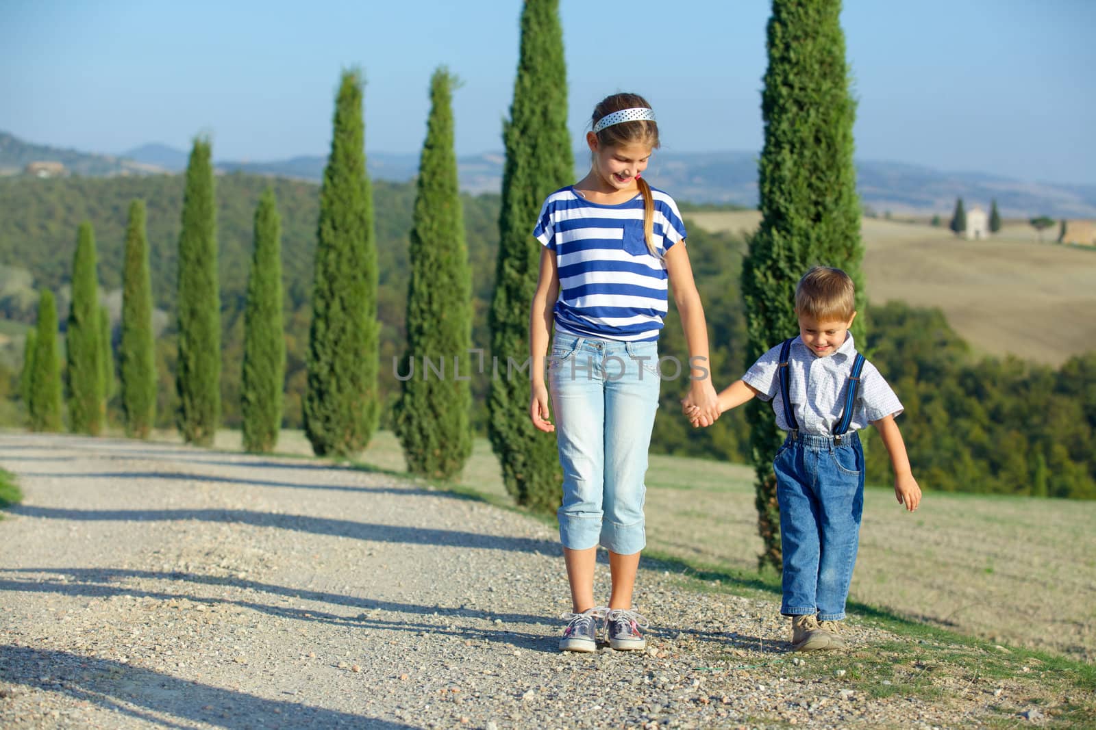 Happy sister and brother having fun on vacations in Tuscan against cypress alley background