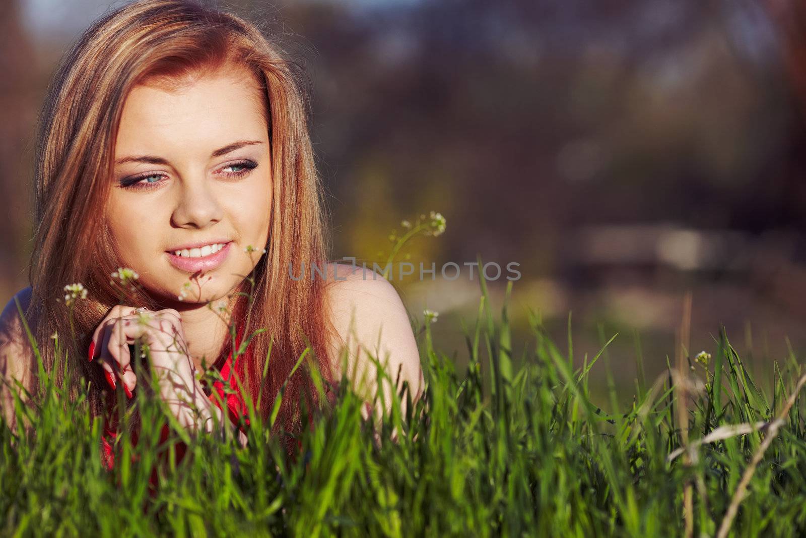 Beautiful woman in a red dress lies on a fresh spring greens