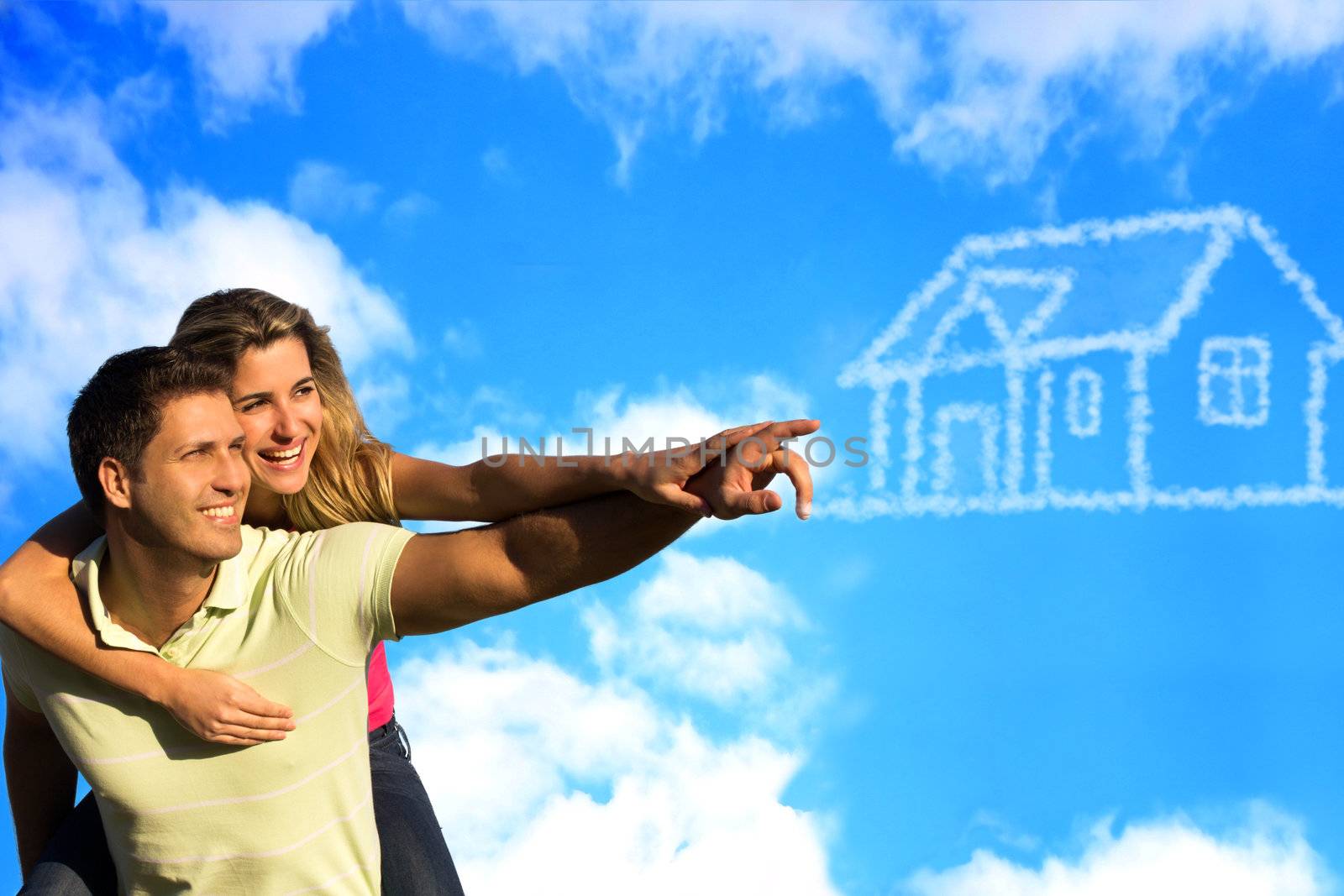 Happy couple under the blue sky enjoying the sun pointing to a house made of clouds.