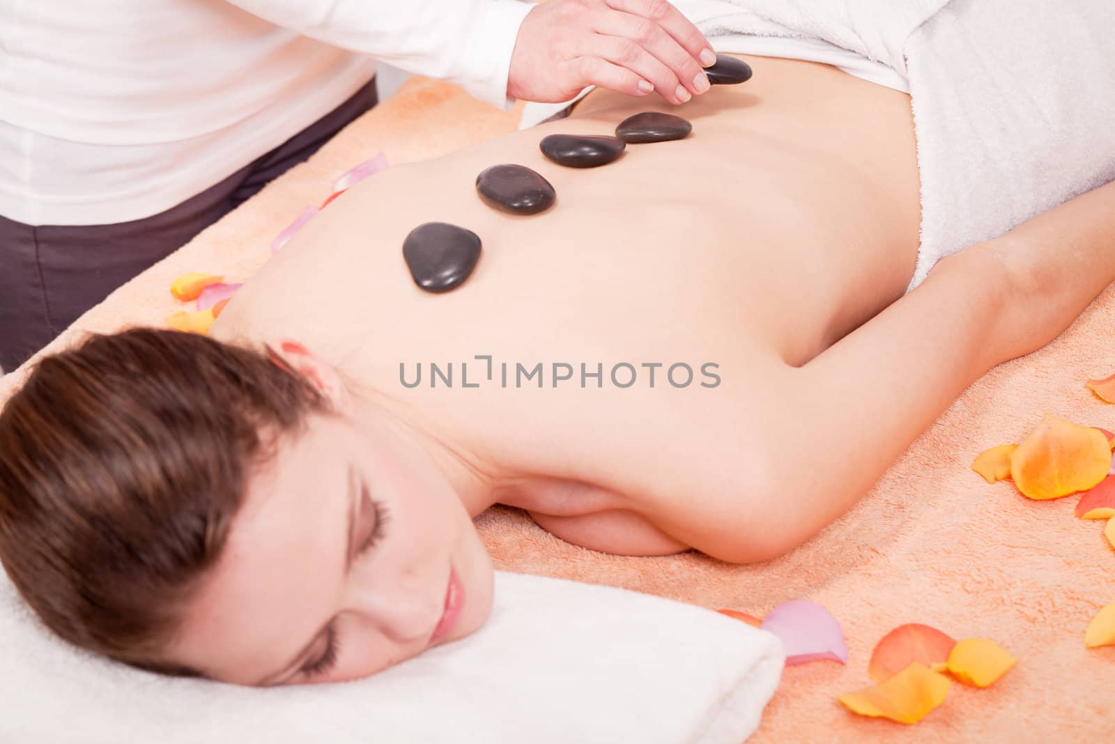 young attractive woman get hot stone massage by professional in wellness spa salon