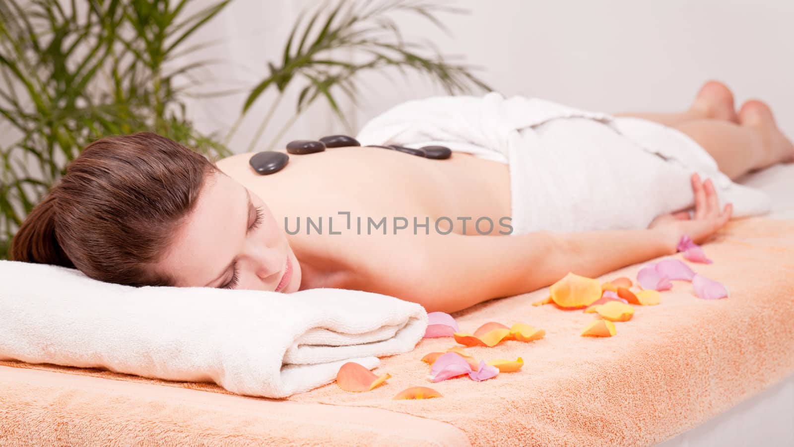 young attractive woman get hot stone massage by professional in wellness spa salon