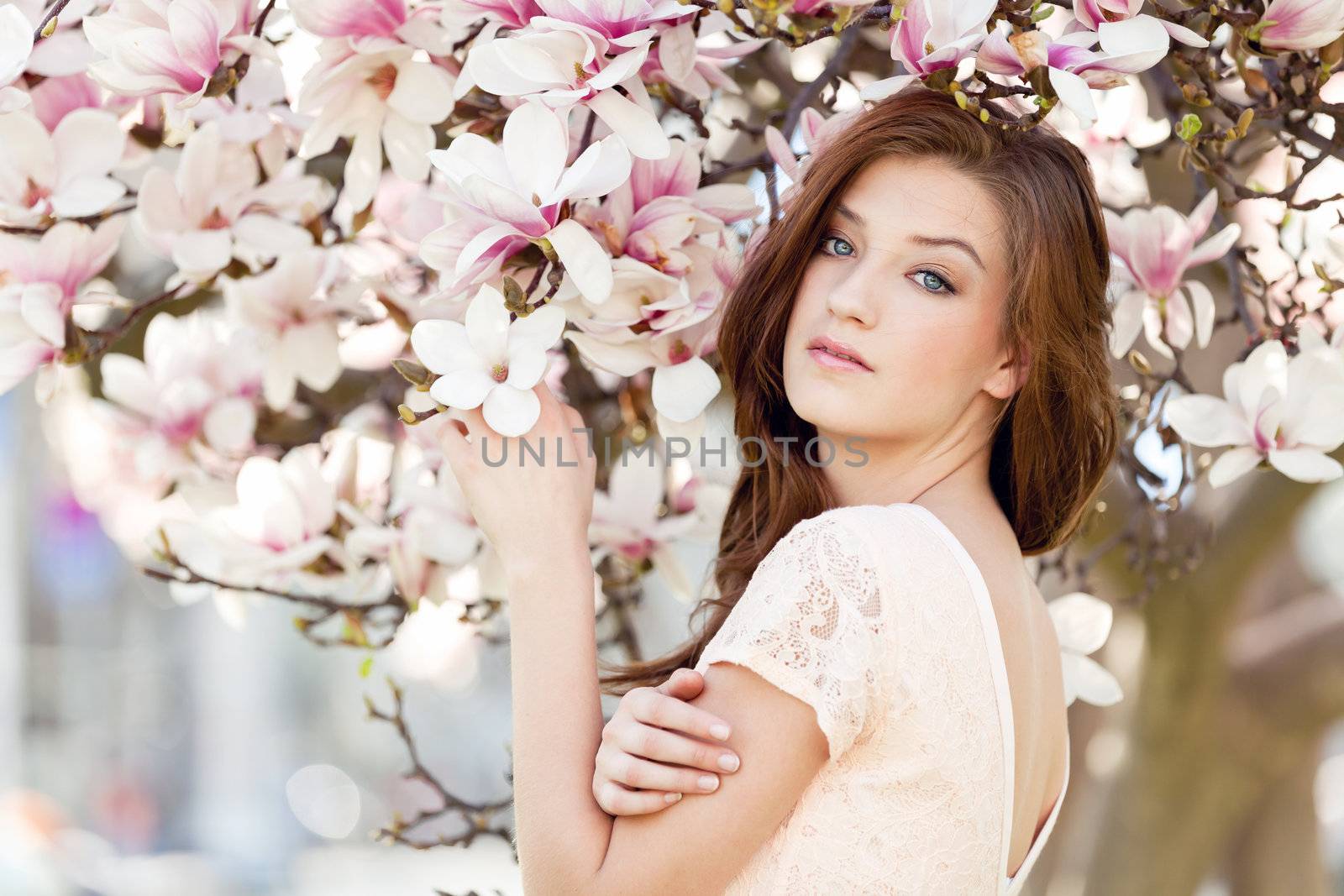 beautiful smiling woman and pink magnolia outside in spring