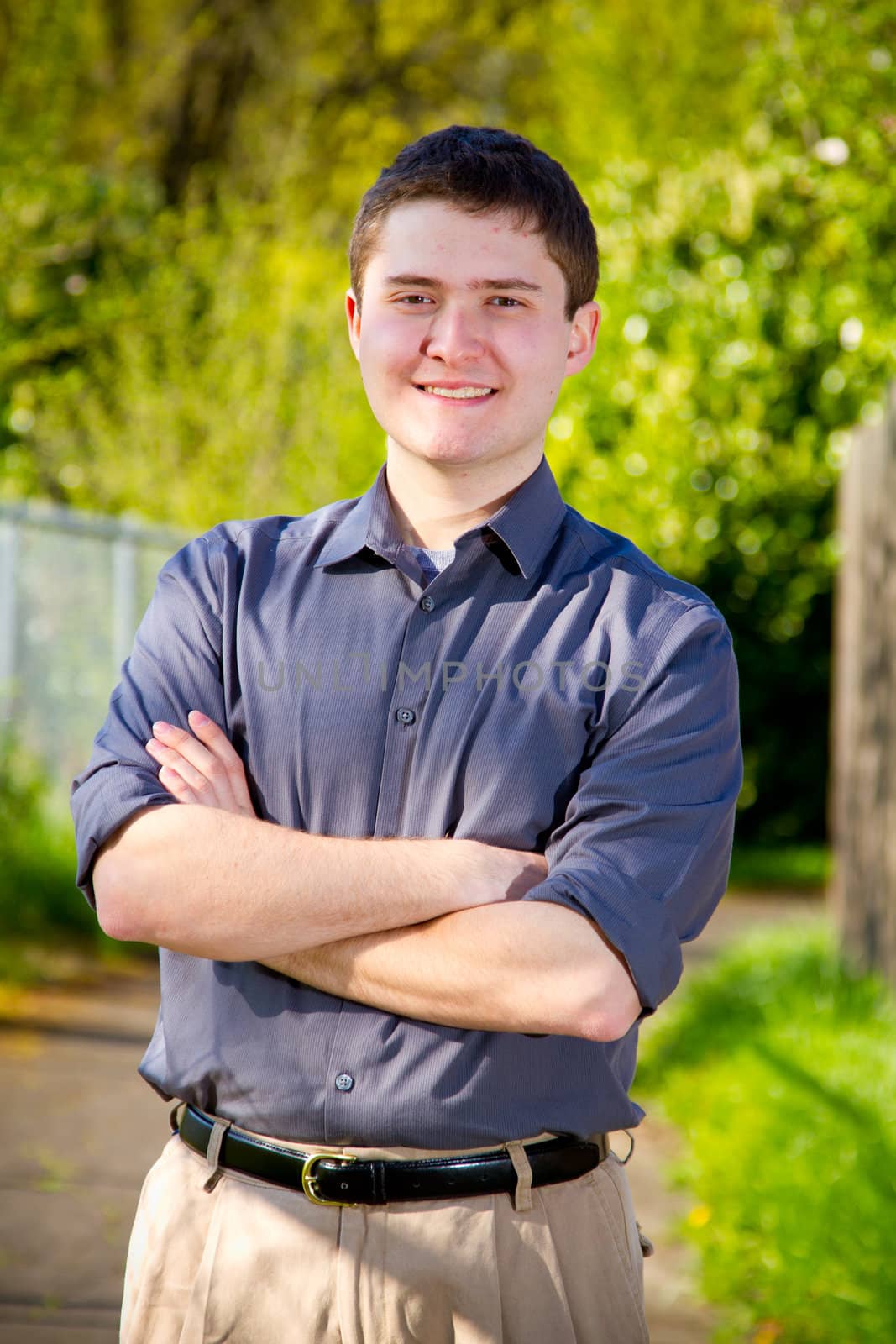 A college student business professional is photographed outside with natural light to create a portrait of a person wearing a grey shirt looking confident.