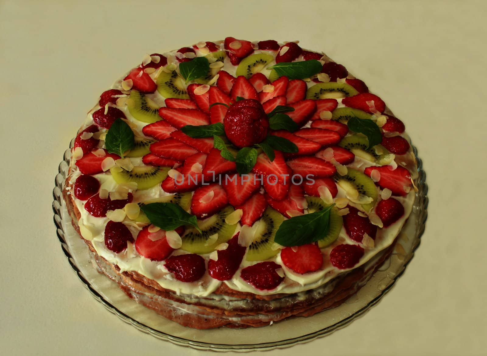 cake with cream filling covered with strawberries kiwi and mint green and almonds. close to