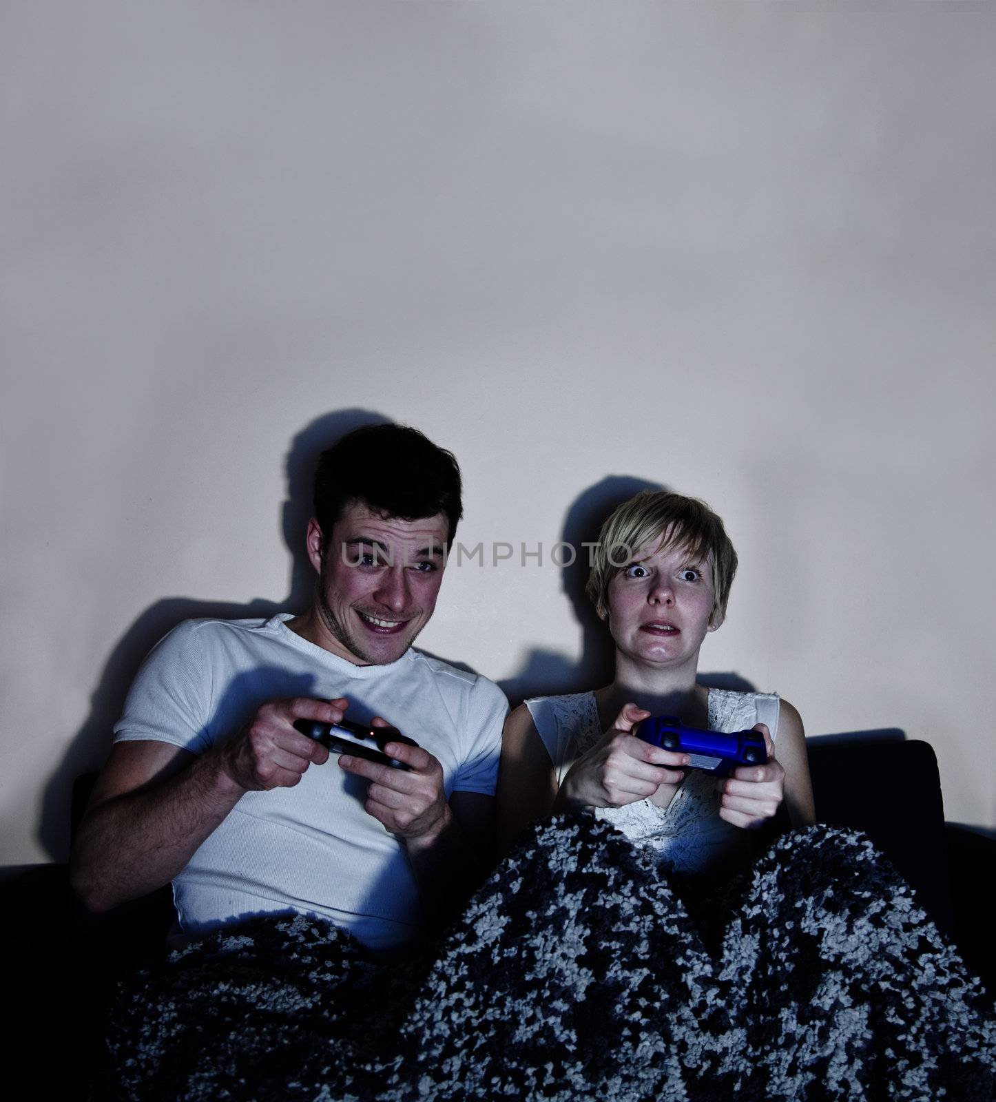 Young couple playing video games comfortably wrapped in a blanke by aetb