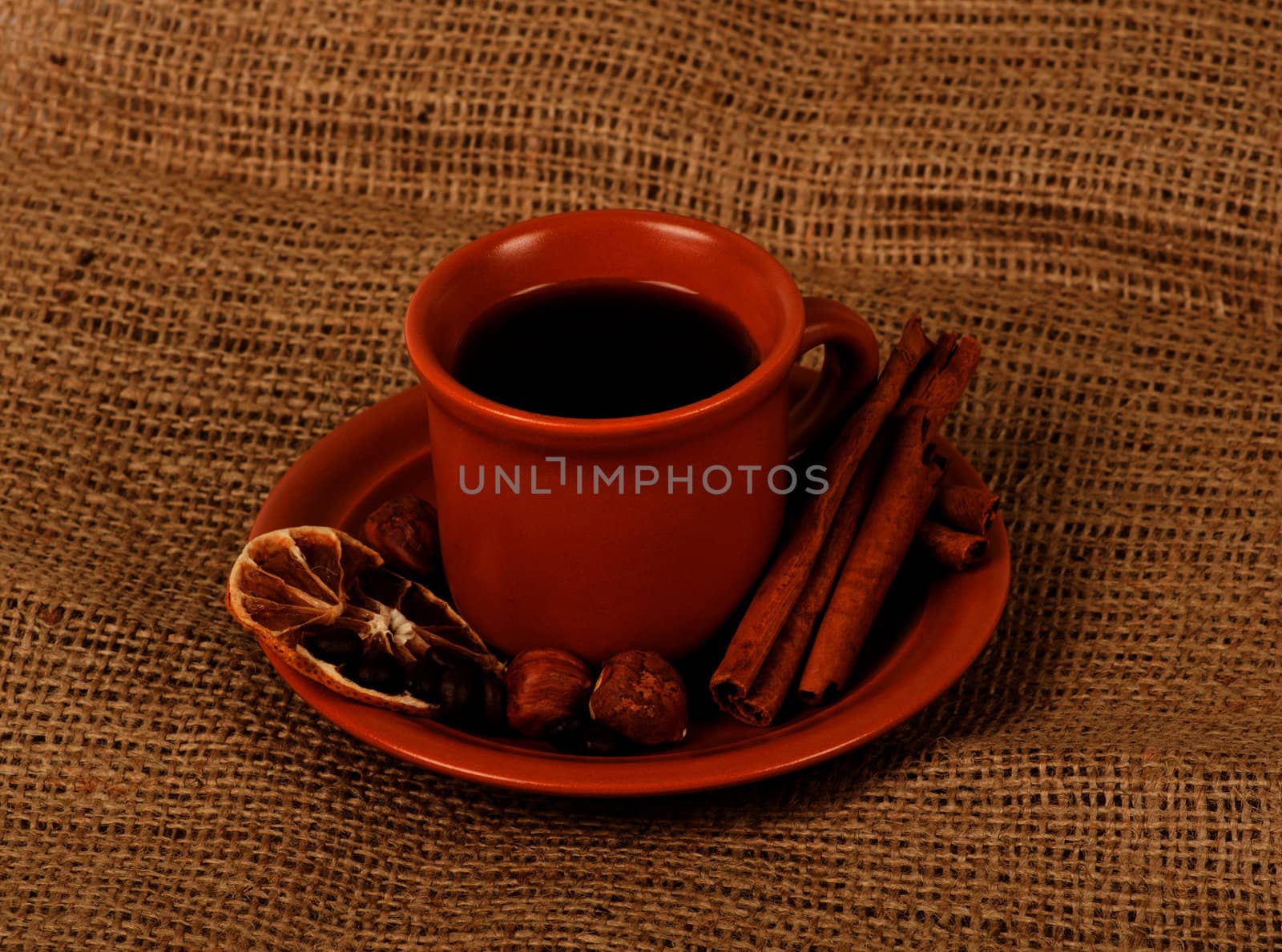 Closeup shot of freshly prepared cup of italian espresso with cinnamon, coffe beans, nuts and lemon over sacking