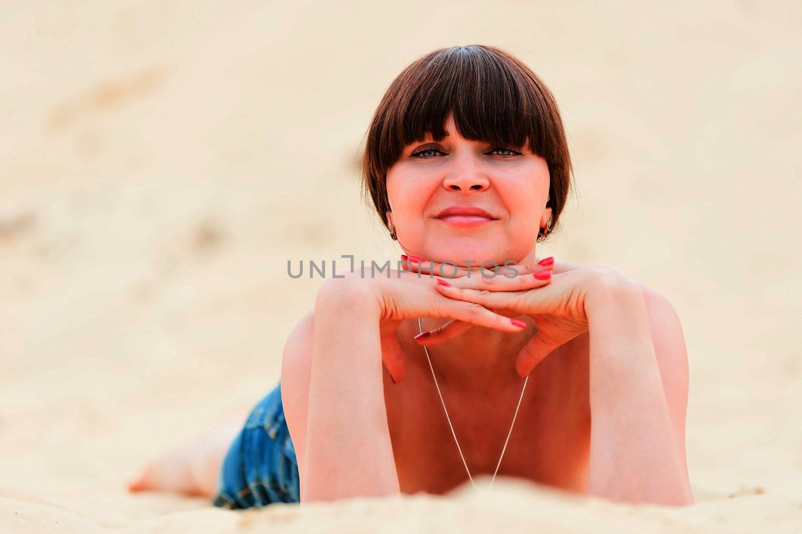 Girl in denim shorts tan while lying on the sand