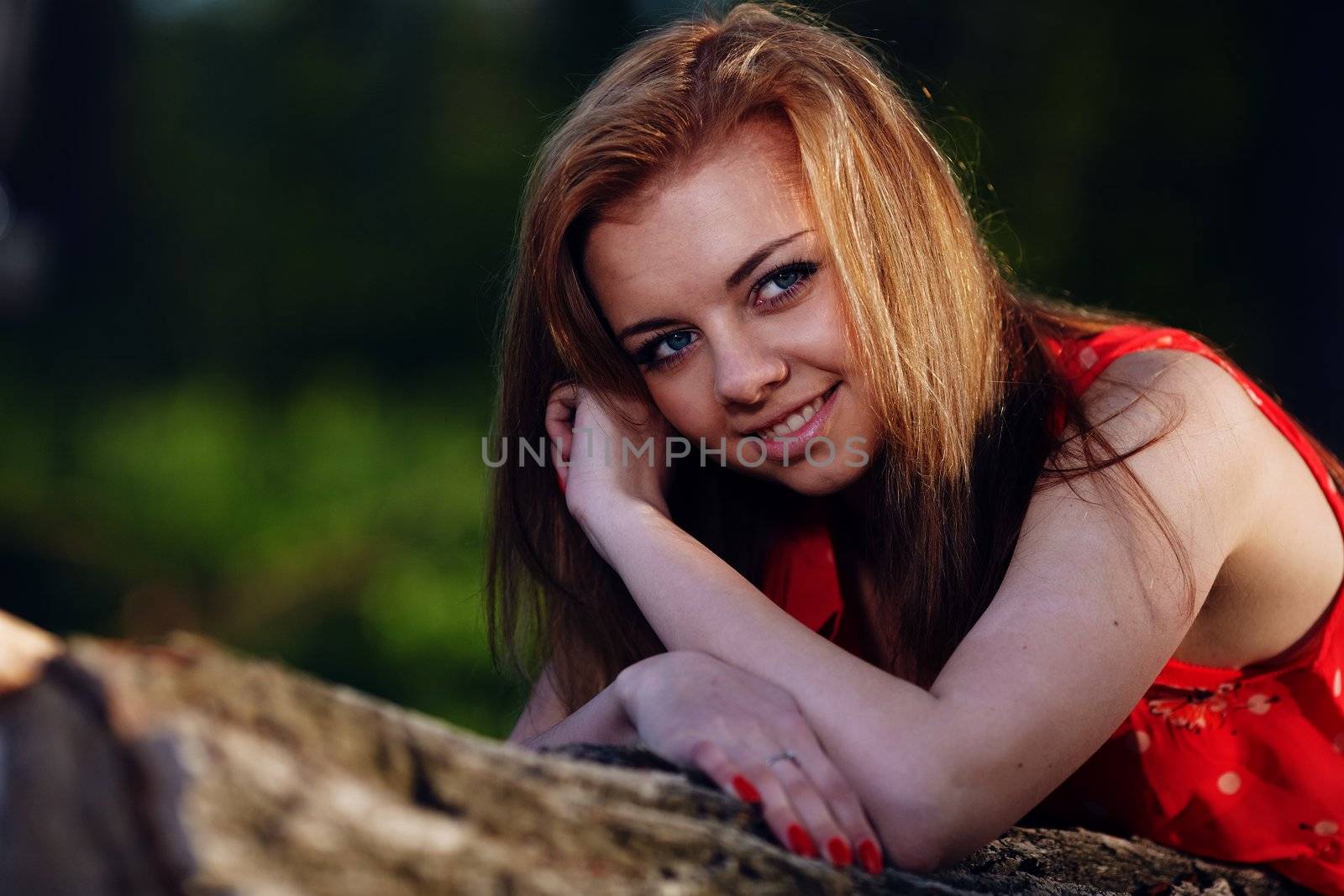 Beautiful girl in a red dress, lying on a log