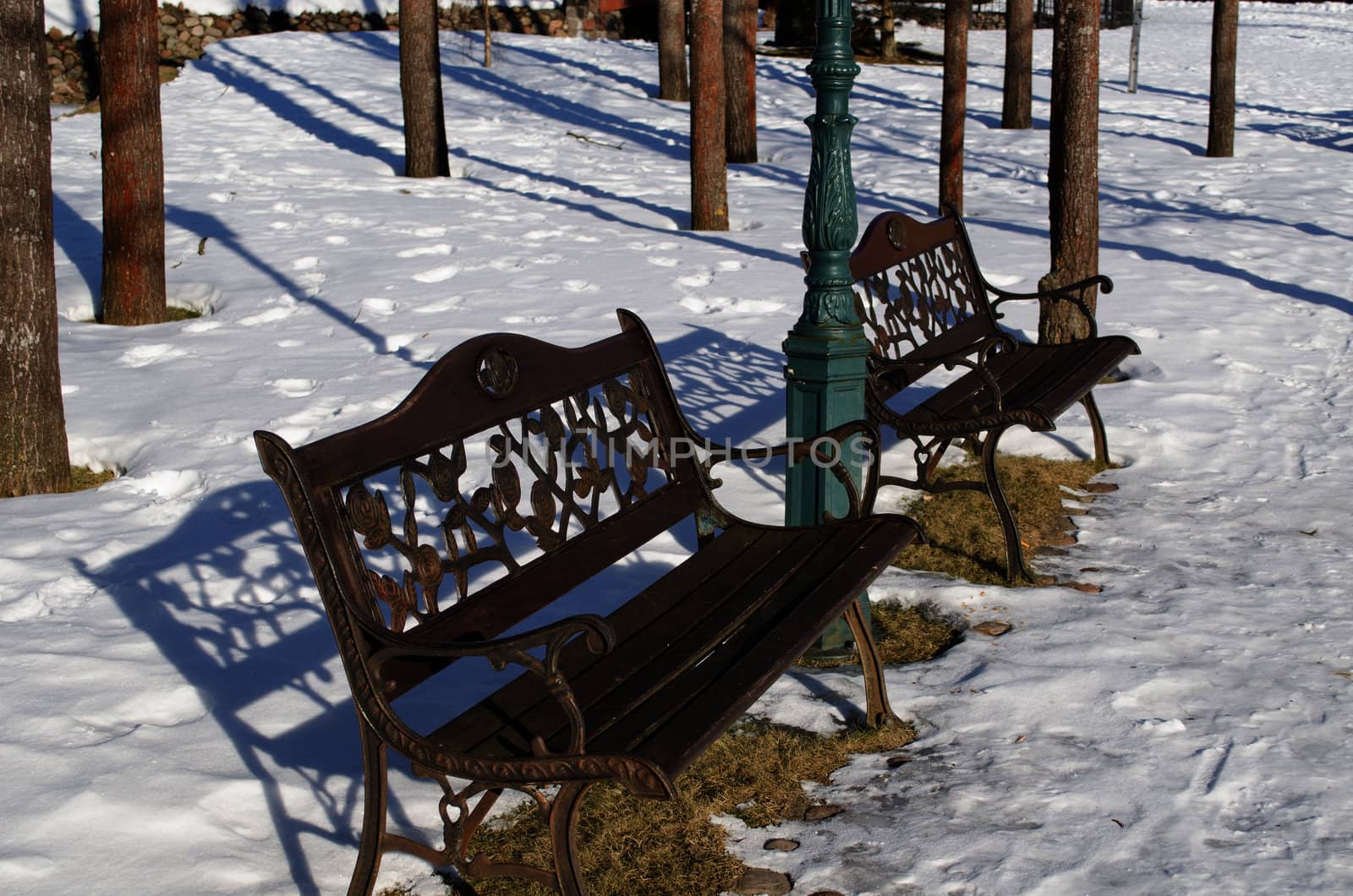 retro decorative benches shadows in park and lighting pole surrounded by snow in winter.