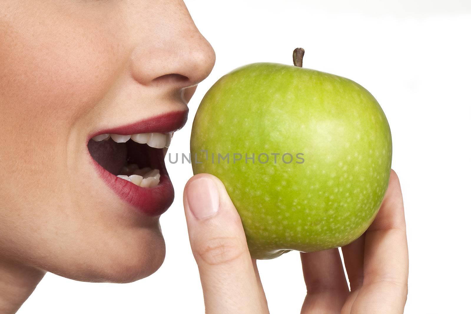 The apple is emphasised in the closeup studio shot of a women about to bite into an fresh apple.