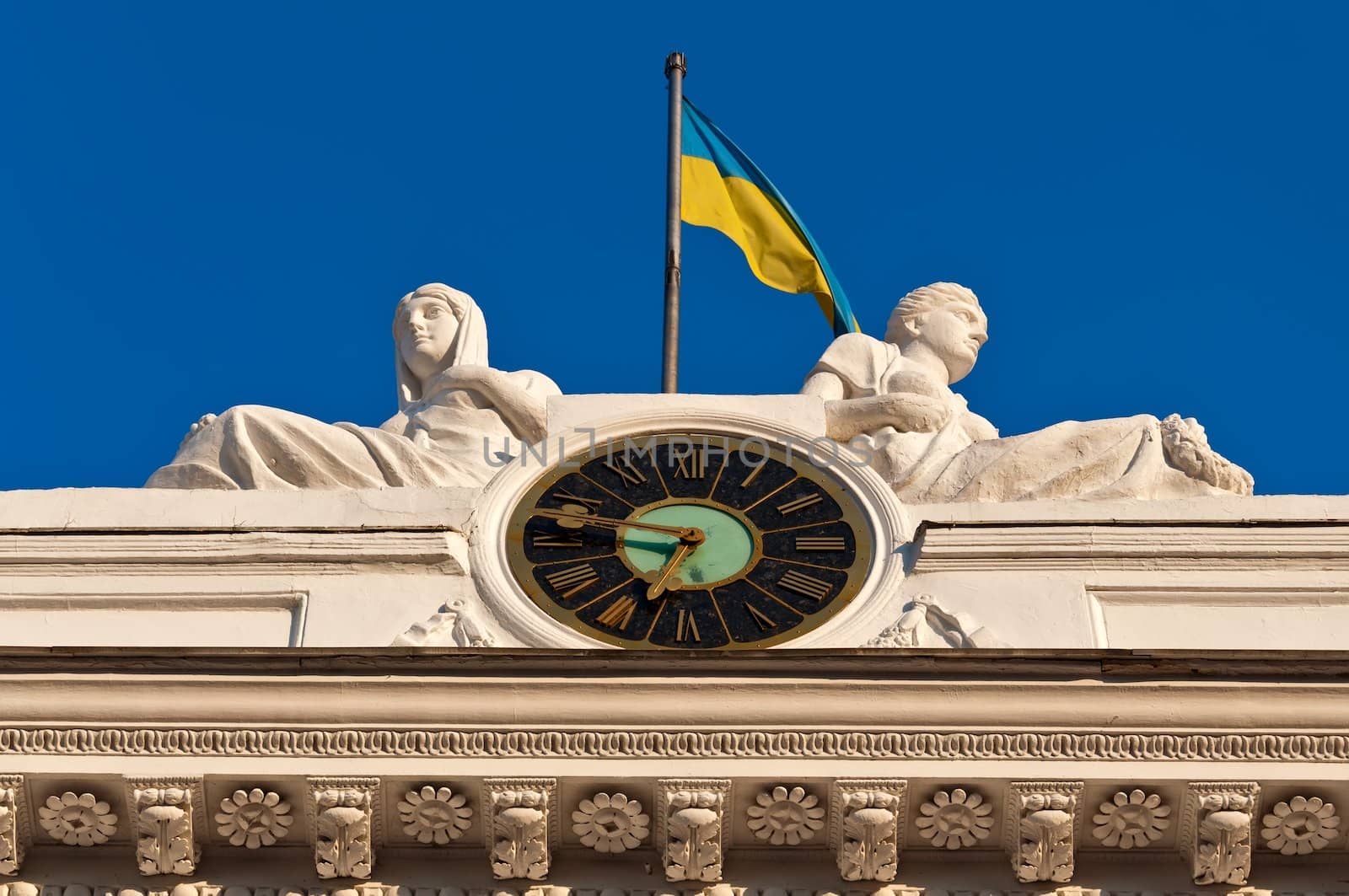 Fragment of a facade of a building of the Odessa city council - chiming clock, sculptural composition and a national flag of Ukraine.