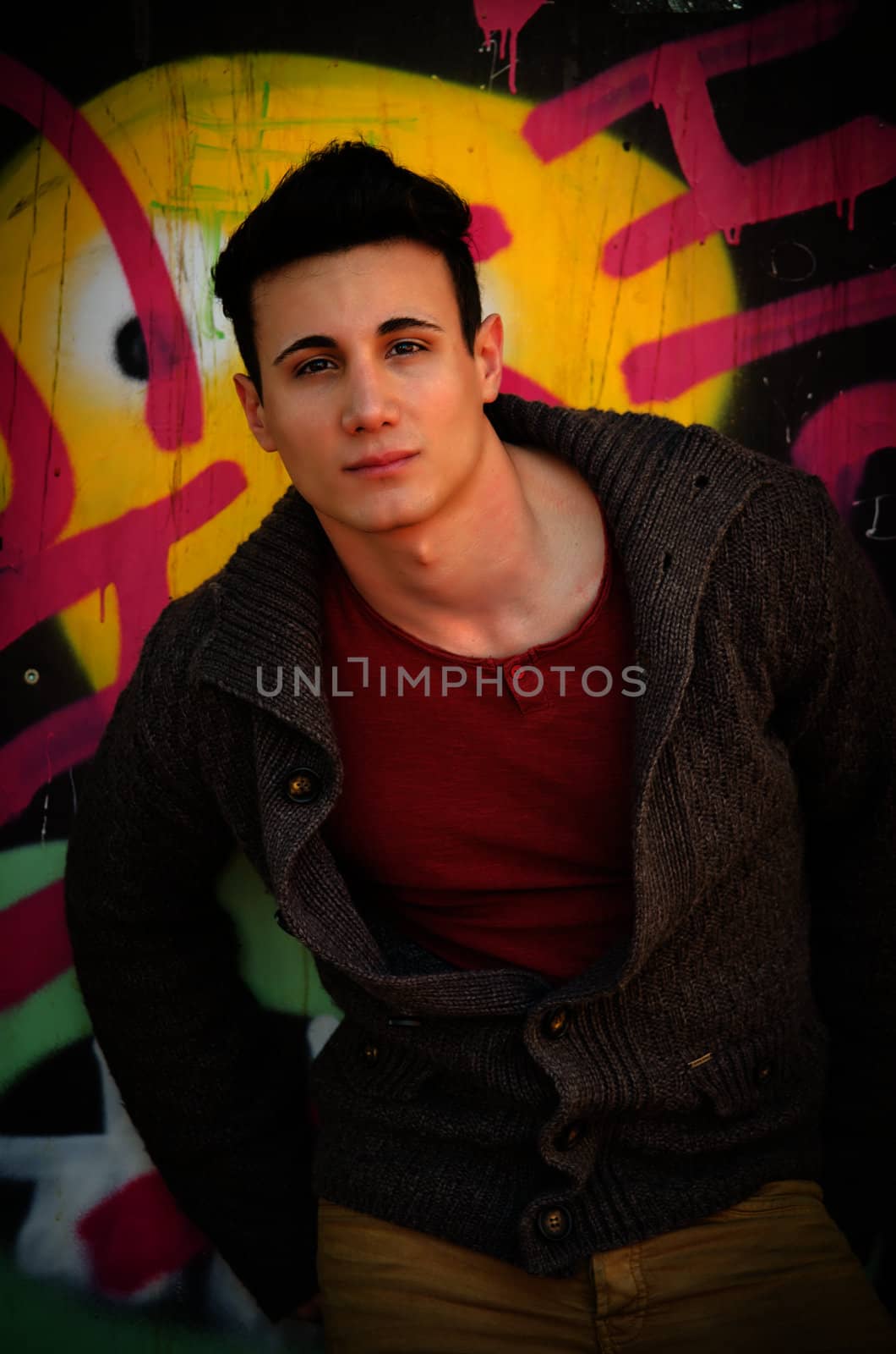 Attractive young man standing outdoors in front of graffitti covered wall