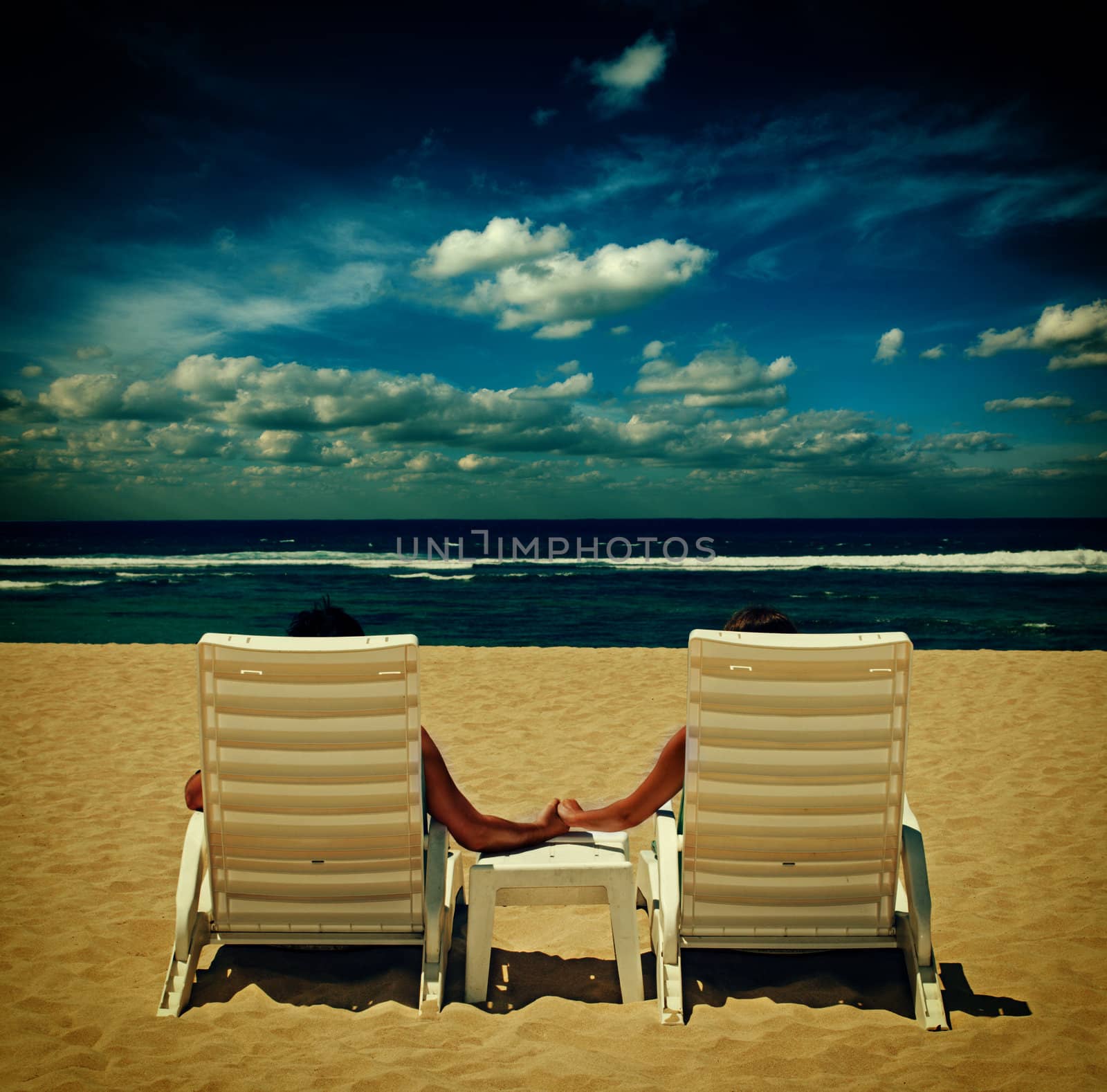 Couple in beach chairs holding hands near ocean