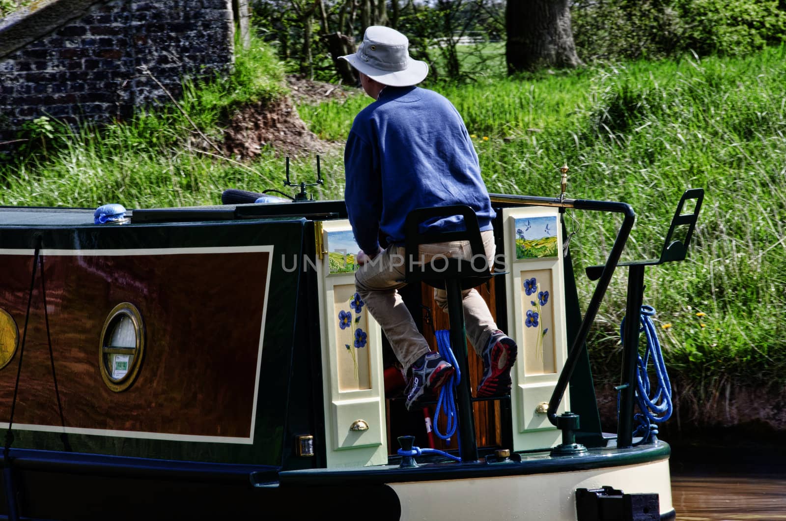 Man sailig a narrowboat along a canal, with pretty painted doors on boat