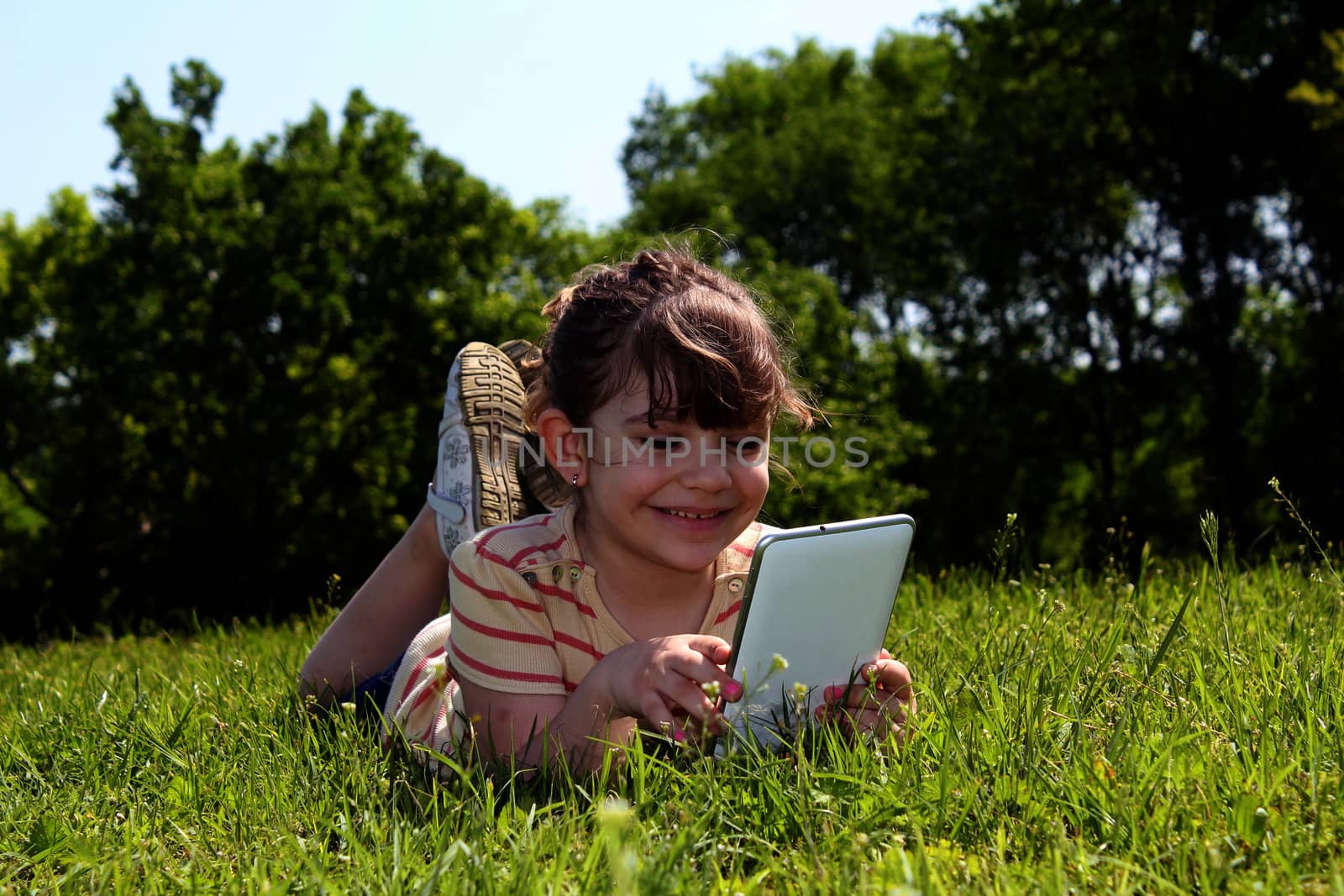 little girl lying on grass and play with tablet pc by goce