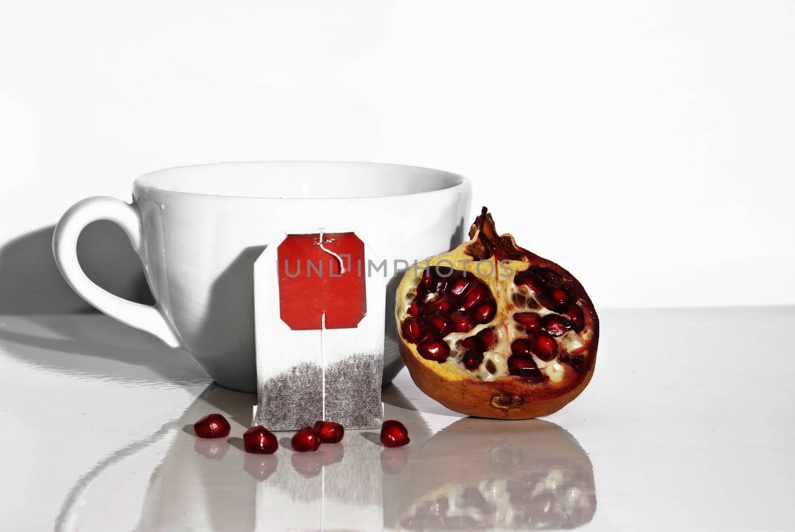 Juicy pomegranate and tea bag on white background
