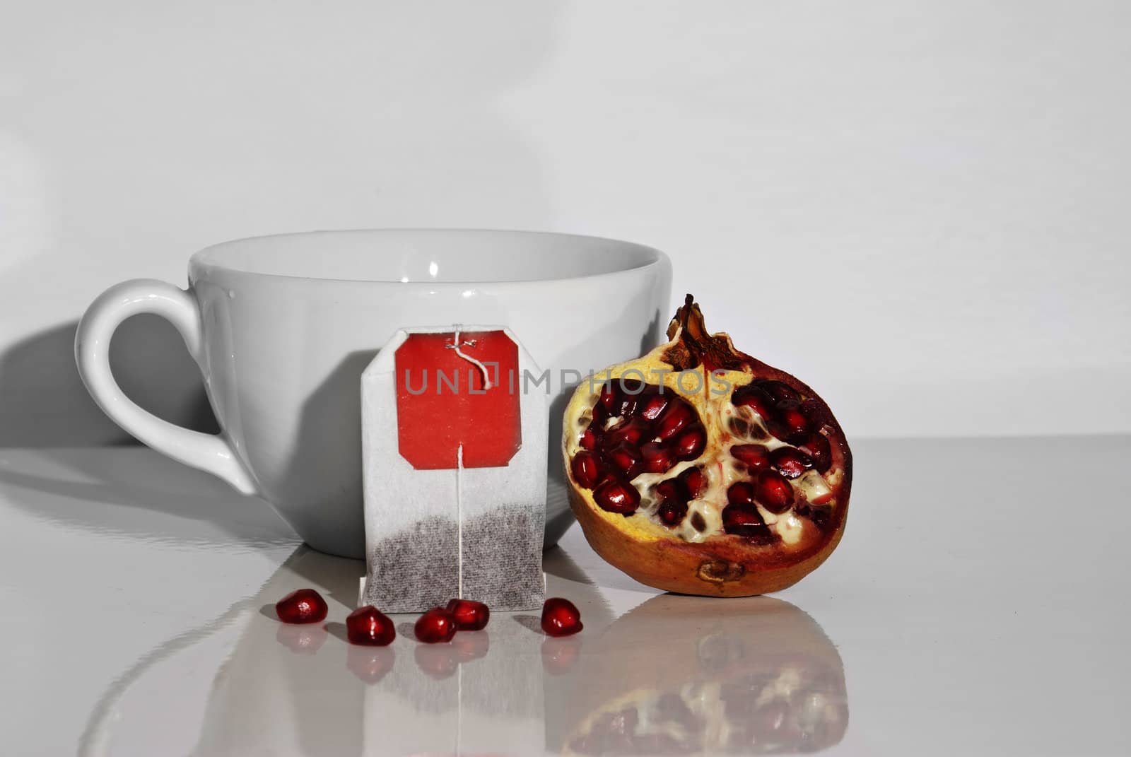 Juicy pomegranate and tea bag on white background