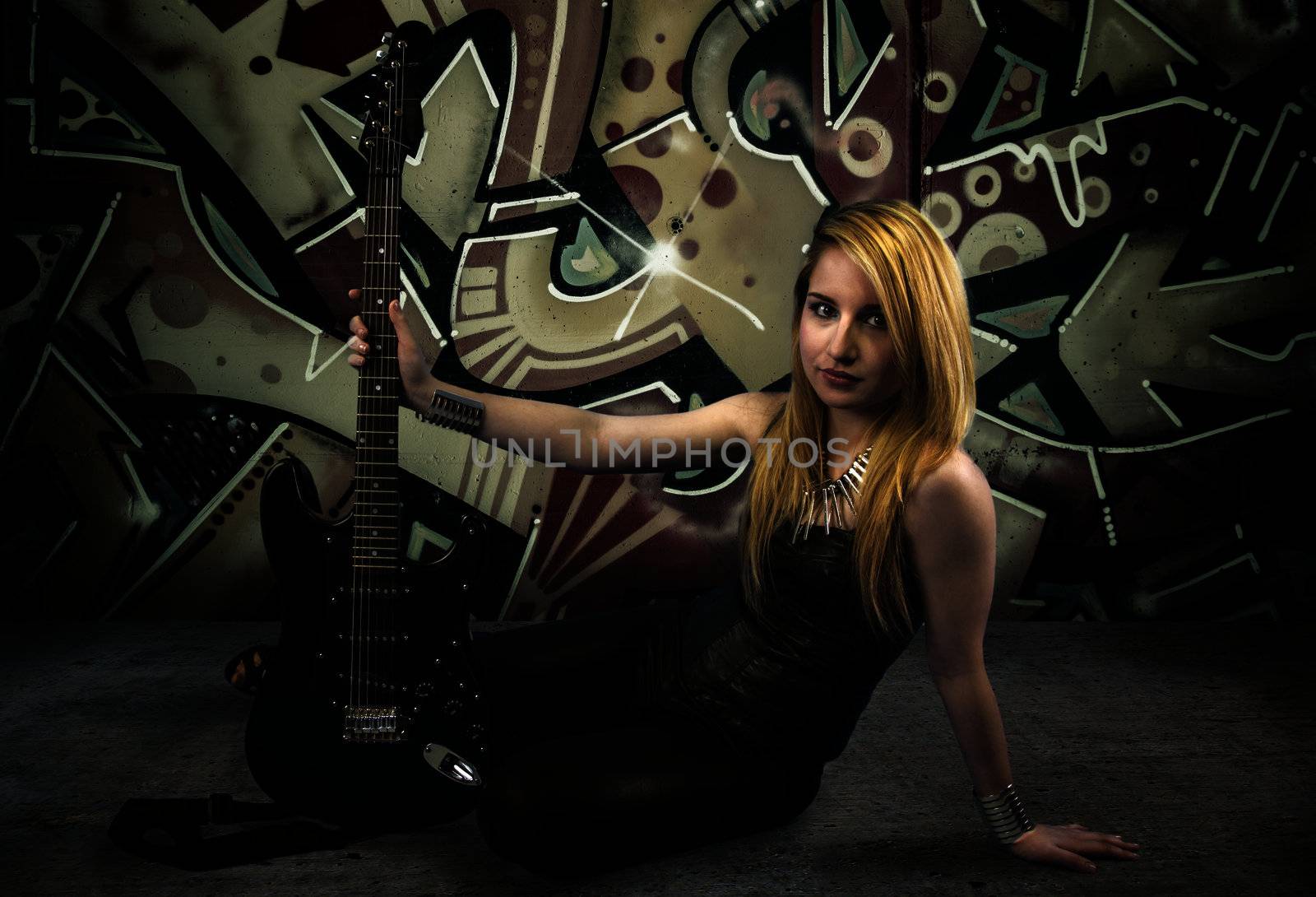 Young blonde holding a black guitar, over grafitti background