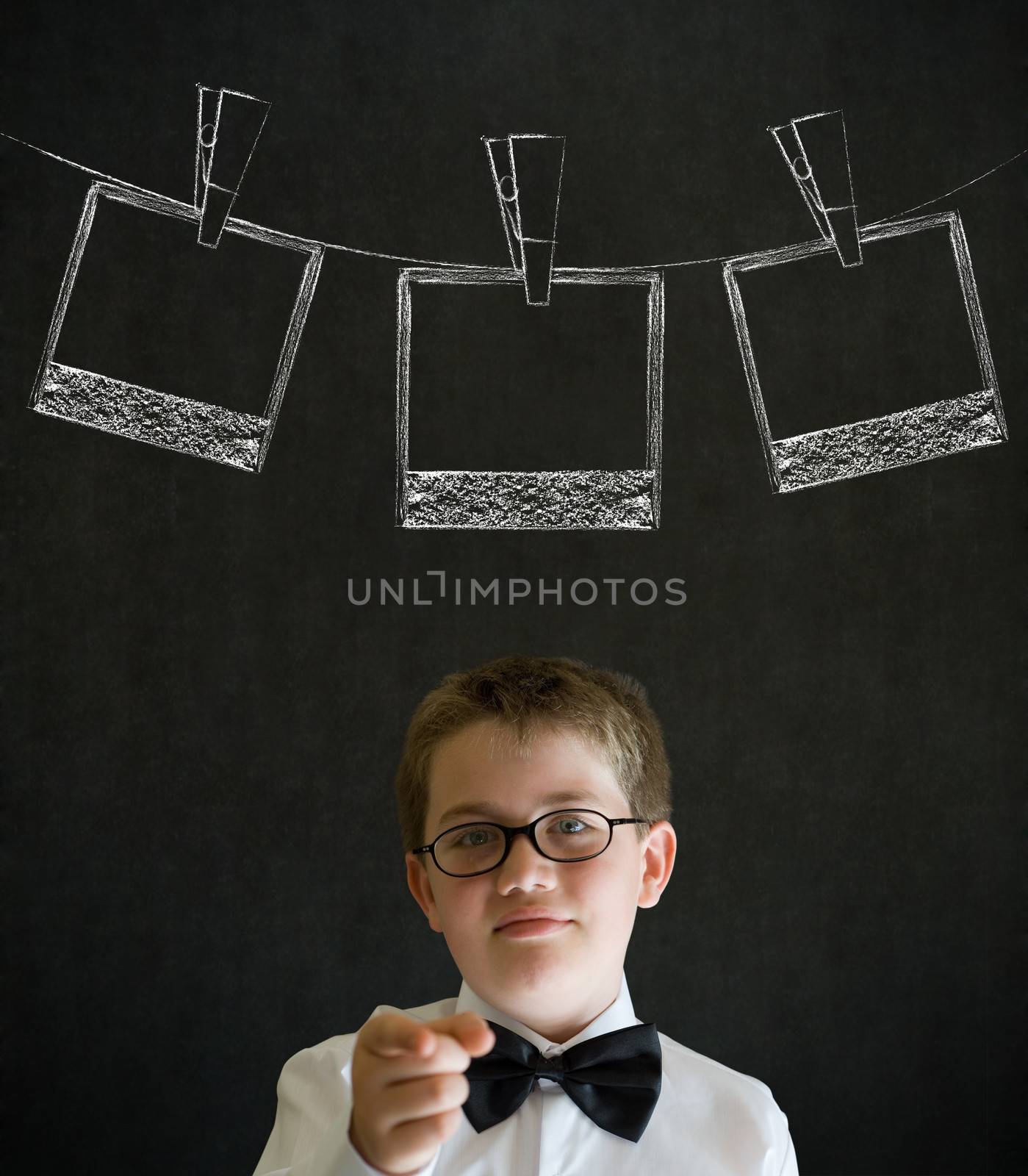 Thinking boy dressed up as business man with hanging instant photograph on blackboard background