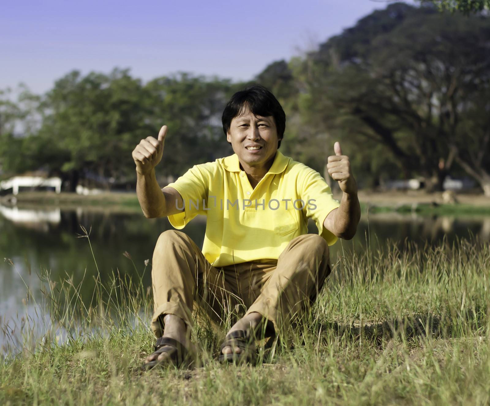 Senior man with thumb up wearing yellow shirt against a green park 