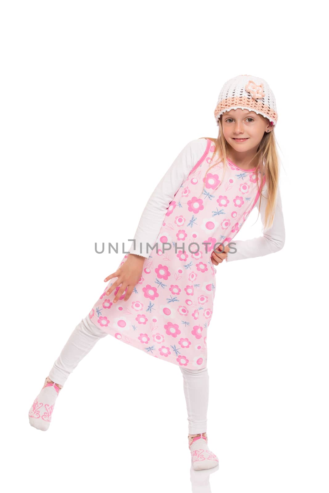Full length portrait of a little girl with long hair wearing summer dress, knit cap and balancing at one leg. Isolated on white background.