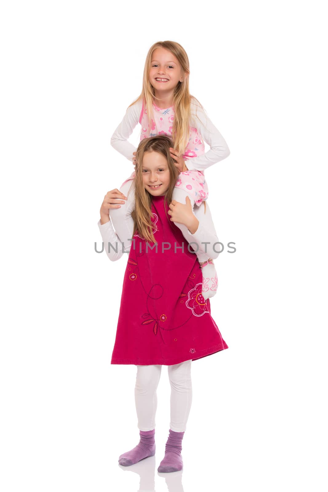 Young girl giving piggyback ride to her sister. Isolated on white background.