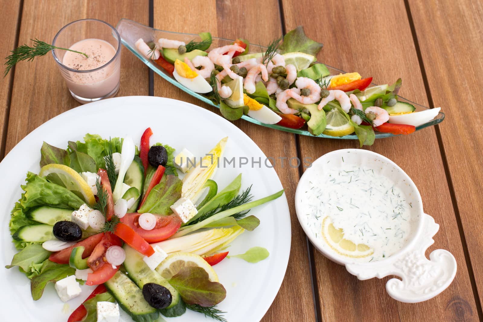 Composition of greek salad and shrimp cocktail on a wooden table.