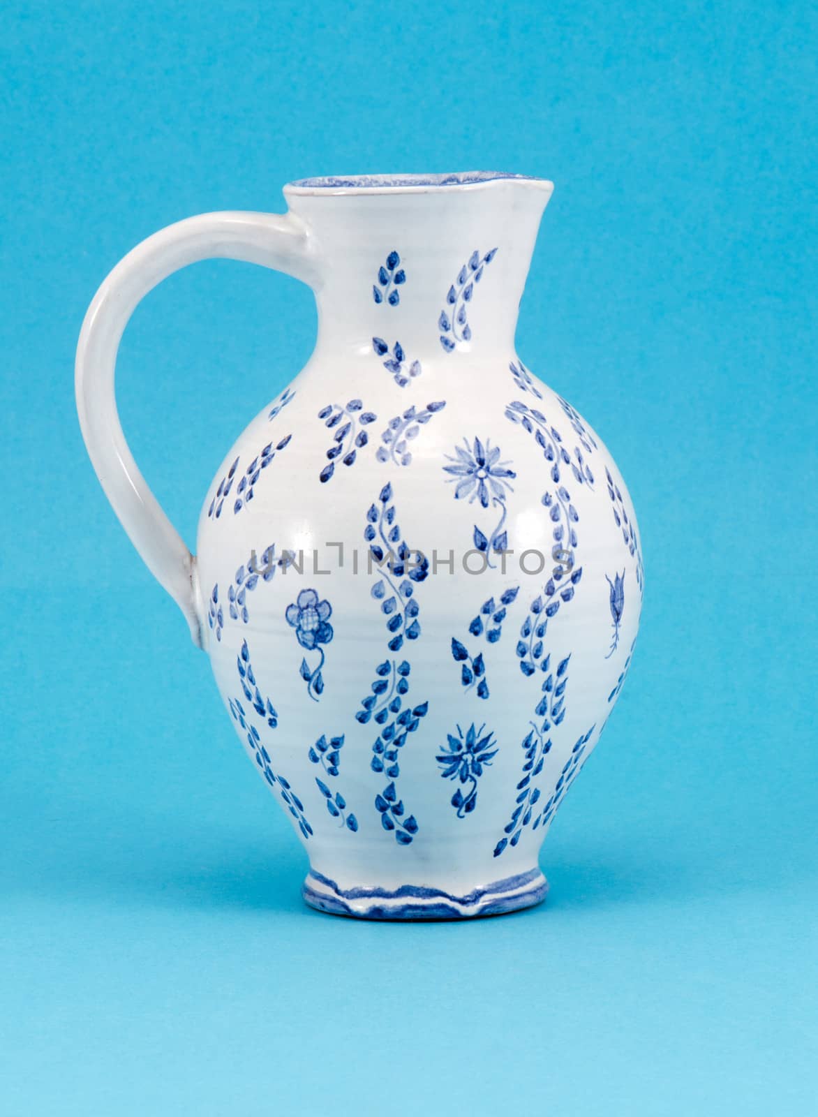 big hand made aged jug jar with art paint ornaments on blue background.