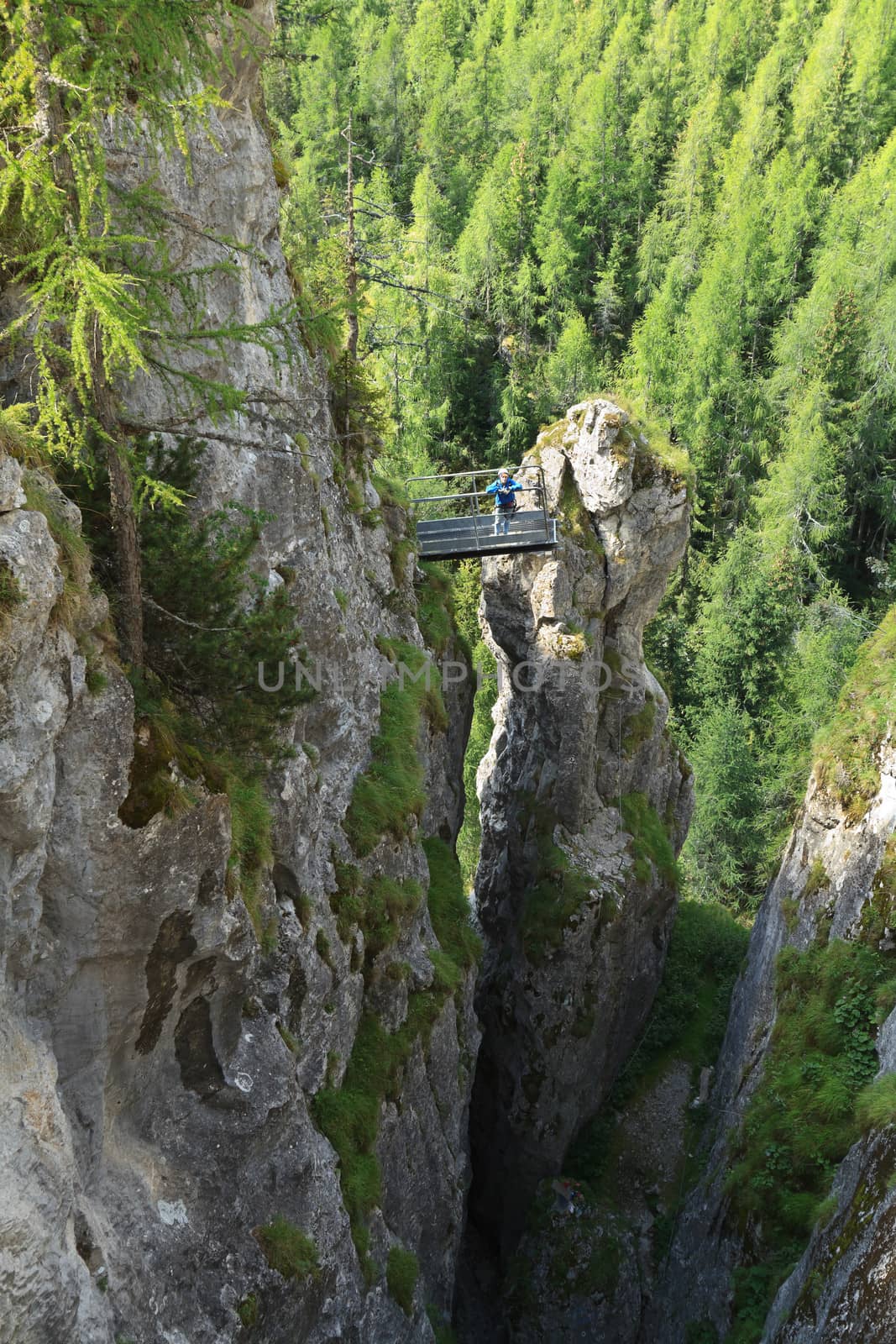 woman on via ferrata Sass de rocia with a metal bridge on top of a monolith, Italian Dolomites
