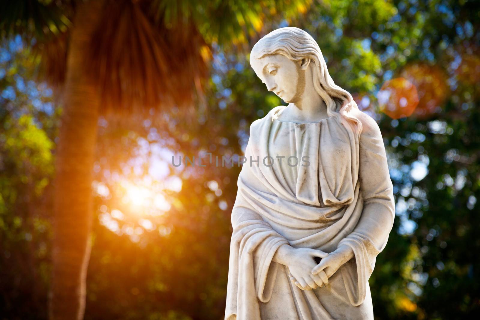 A young woman with folded hands looking down. Sculpture in the park