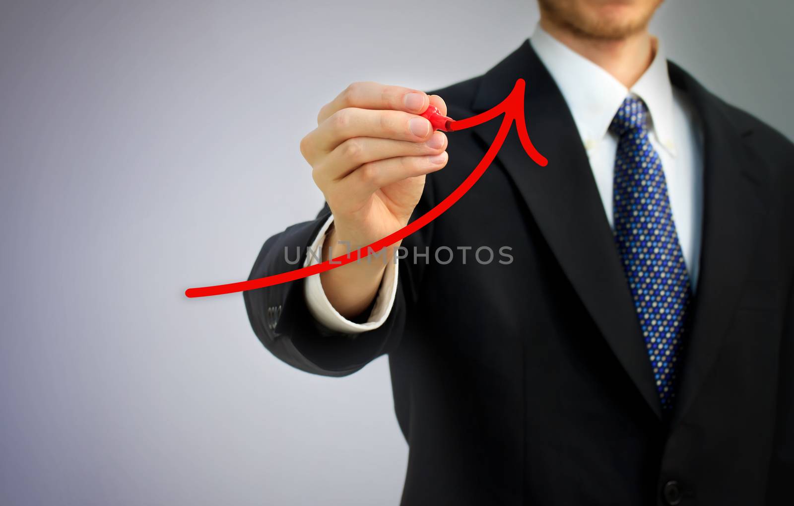 Businessman drawing a red rising arrow over gray background