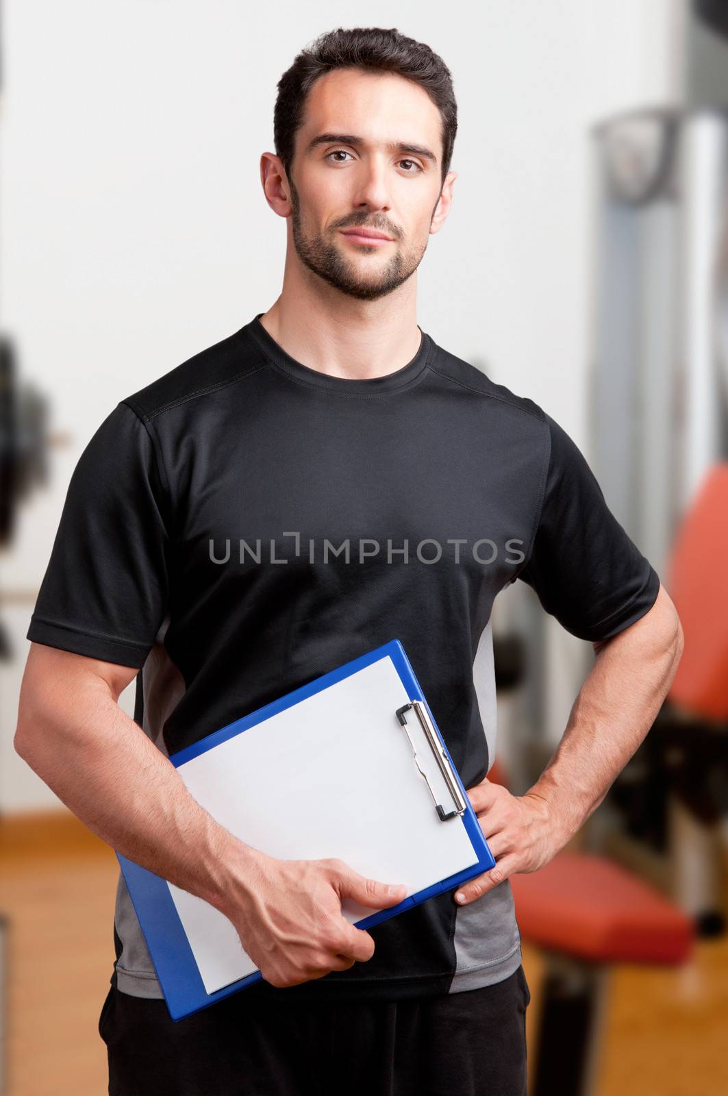 Personal Trainer, with a pad in his hand, in a gym